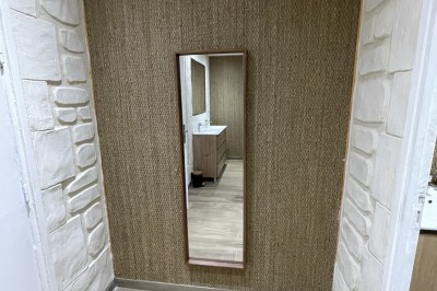 Entrée d'un bâtiment beige avec une toiture rouge, entourée de palissades en bois et d'une pelouse artificielle.