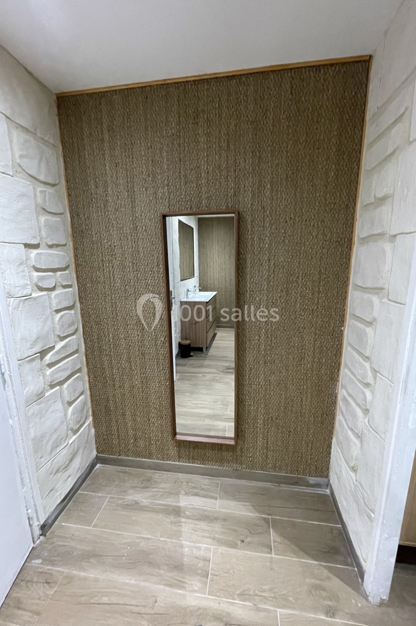 Miroir rectangulaire encadré en bois fixé sur un mur texturé, avec un sol en carrelage et un meuble de salle de bain visible…