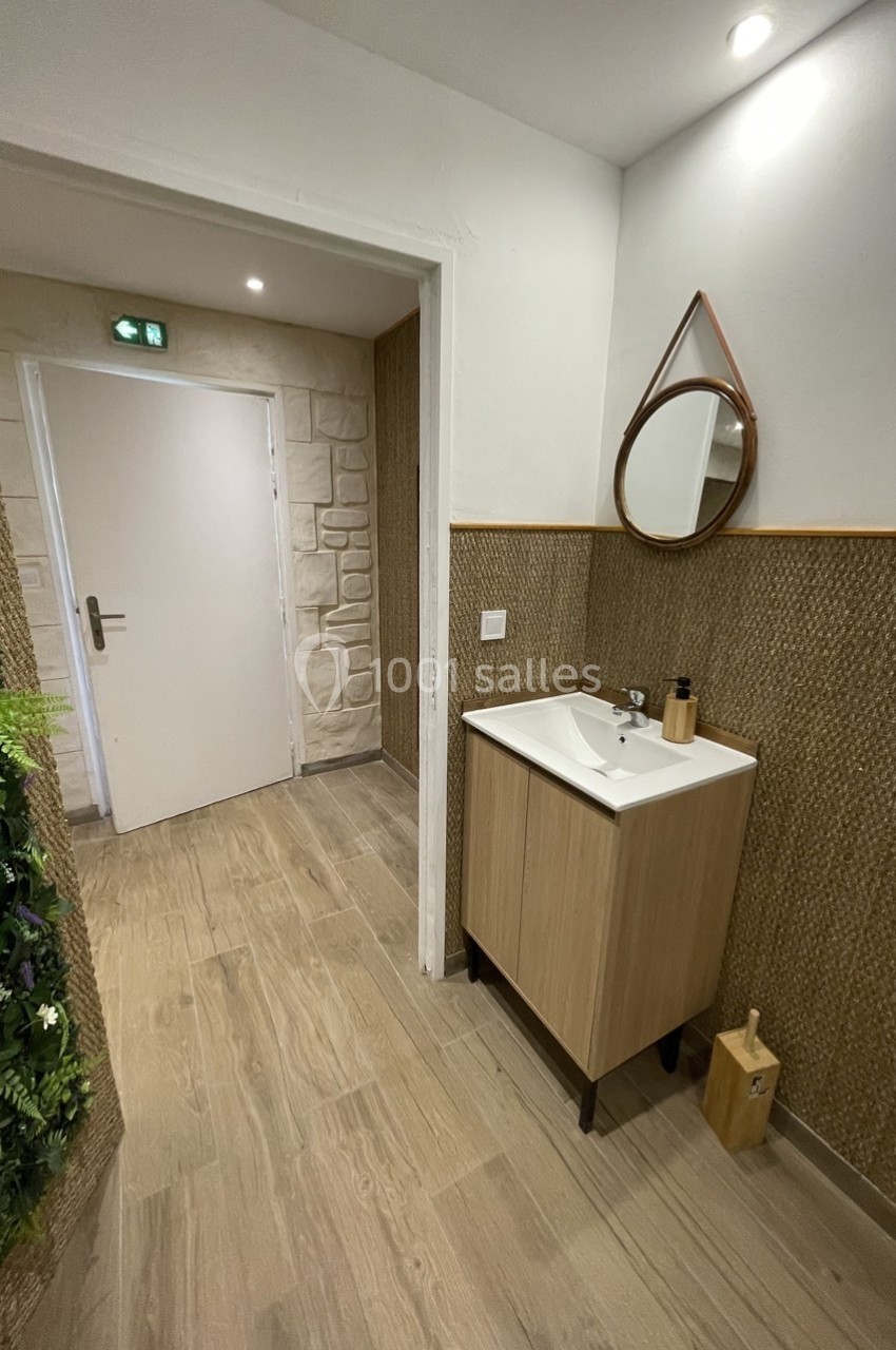 Lavabo avec miroir mural dans un espace aux murs texturés, sol en bois et décoration végétale.