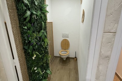 Entrée d'un bâtiment beige avec une toiture rouge, entourée de palissades en bois et d'une pelouse artificielle.