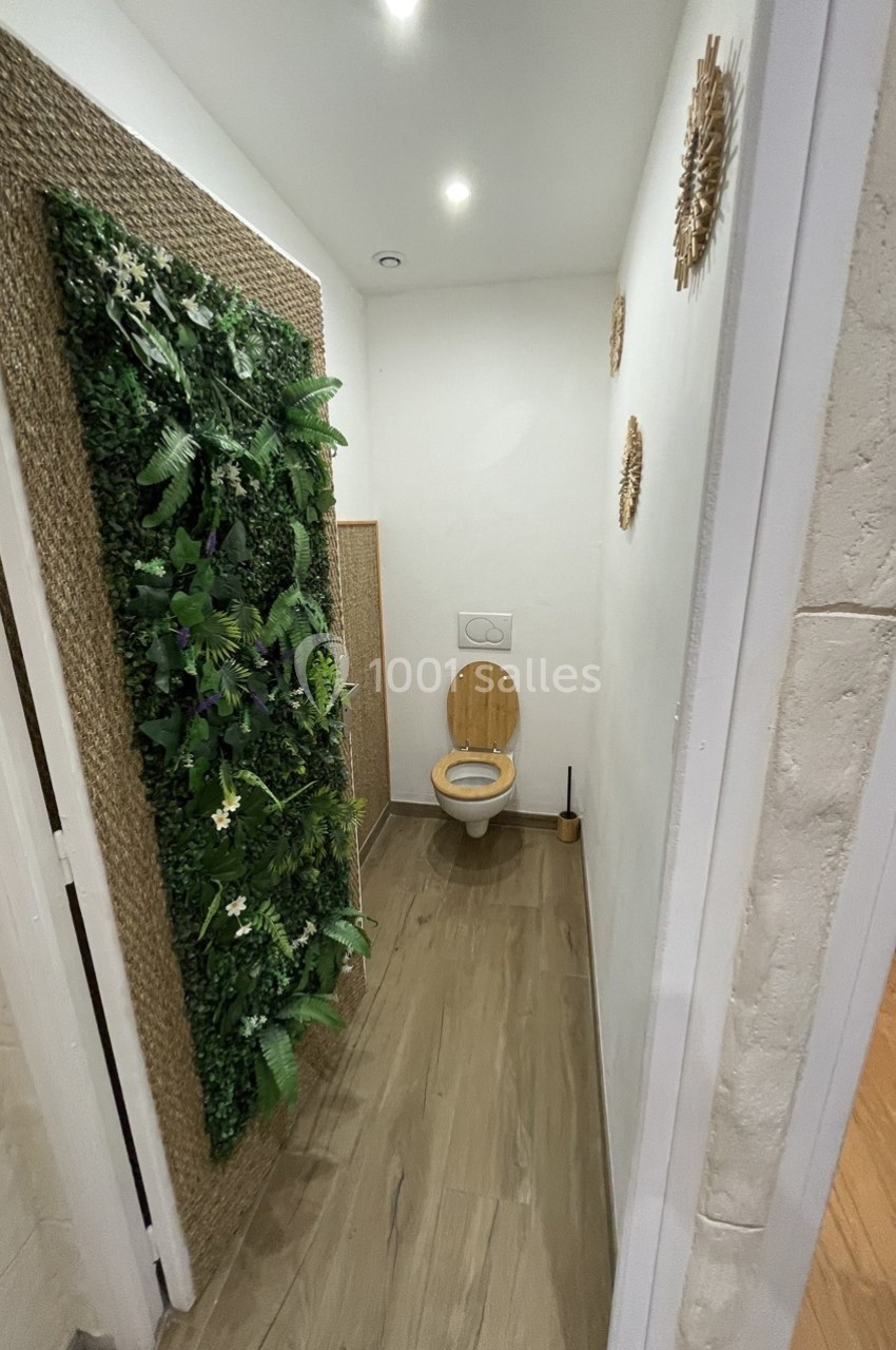 Toilettes avec abattant en bois, mur végétalisé décoratif à gauche et sol en parquet clair.