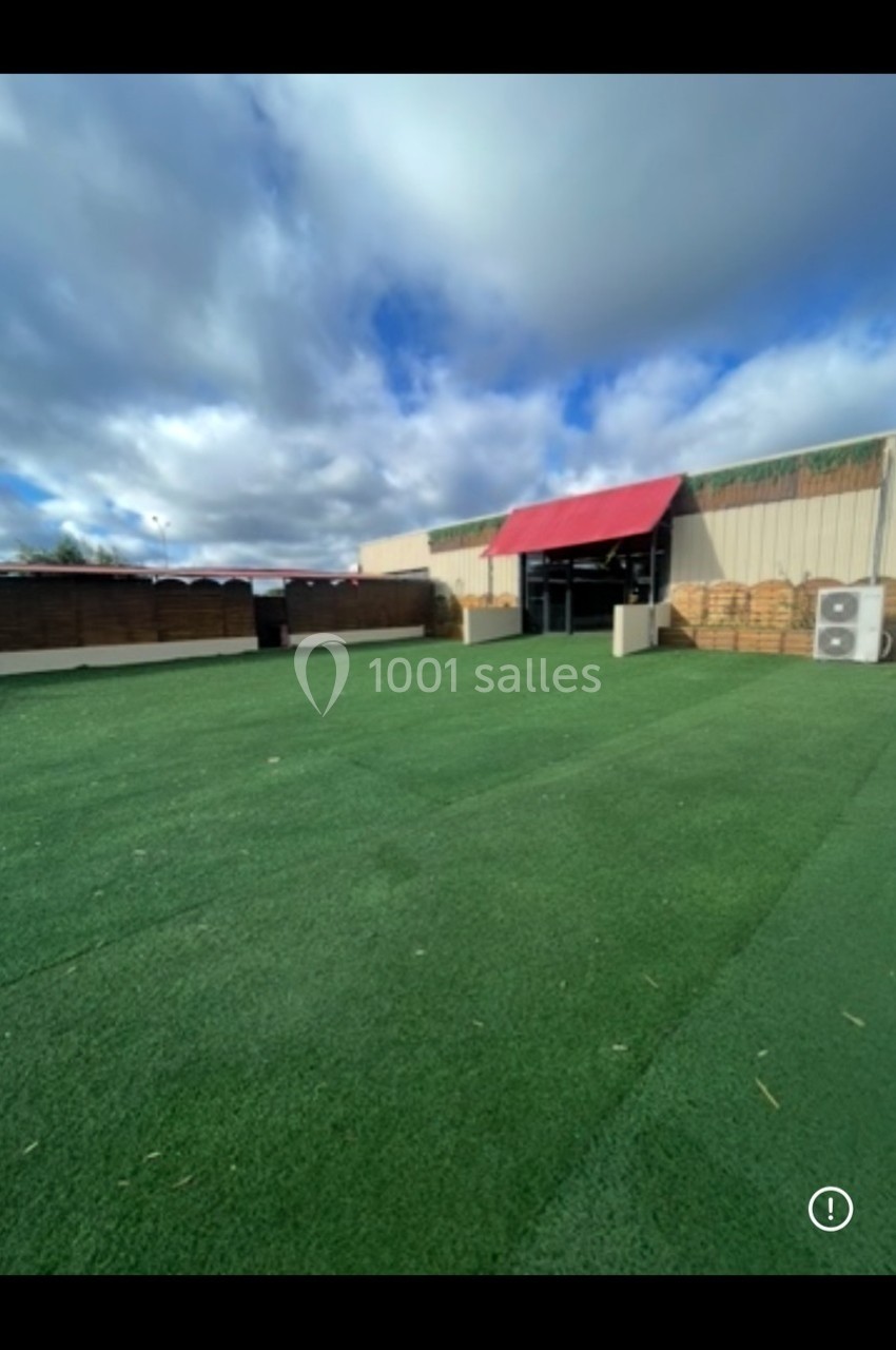 Cour extérieure avec sol en gazon synthétique, entourée de clôtures en bois et d'un bâtiment avec auvent rouge.