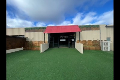 Entrée d'un bâtiment beige avec une toiture rouge, entourée de palissades en bois et d'une pelouse artificielle.