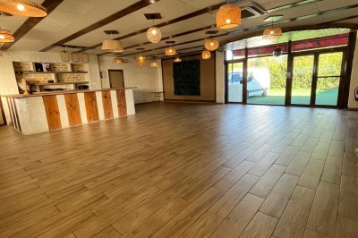 Salle lumineuse avec parquet en bois, mur végétal, chaises empilées et suspensions décoratives au plafond.
