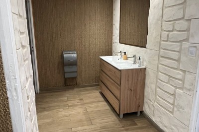 Salle lumineuse avec parquet en bois, mur végétal, chaises empilées et suspensions décoratives au plafond.