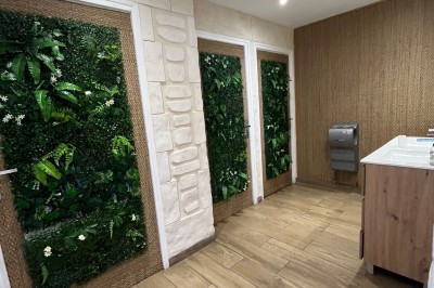 Salle lumineuse avec parquet en bois, mur végétal, chaises empilées et suspensions décoratives au plafond.