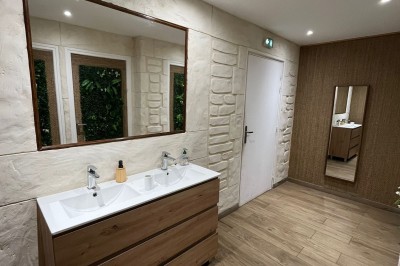 Salle lumineuse avec parquet en bois, mur végétal, chaises empilées et suspensions décoratives au plafond.