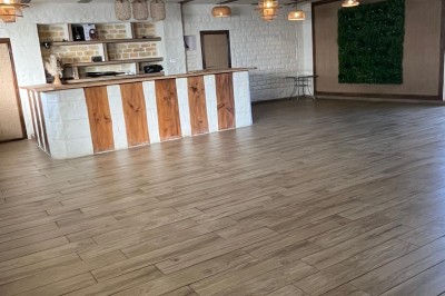 Salle lumineuse avec parquet en bois, mur végétal, chaises empilées et suspensions décoratives au plafond.