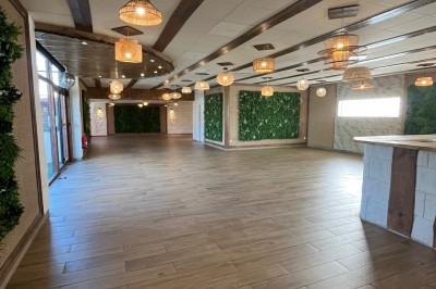 Salle lumineuse avec parquet en bois, mur végétal, chaises empilées et suspensions décoratives au plafond.
