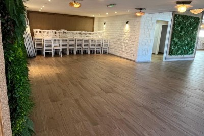 Salle lumineuse avec parquet en bois, mur végétal, chaises empilées et suspensions décoratives au plafond.