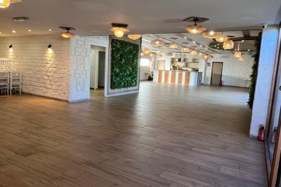 Salle lumineuse avec parquet en bois, mur végétal, chaises empilées et suspensions décoratives au plafond.