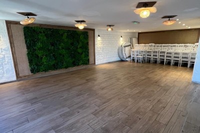 Salle lumineuse avec parquet en bois, mur végétal, chaises empilées et suspensions décoratives au plafond.