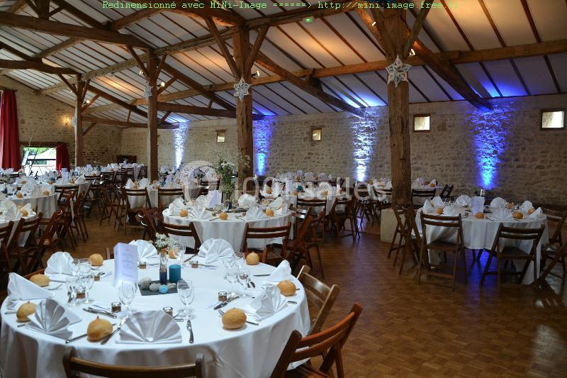 Salle de réception avec tables rondes dressées, nappes blanches, serviettes pliées et éclairage mural bleu.