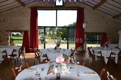 Vue depuis une porte vitrée sur un jardin avec des tables hautes et des chaises disposées près d'un bâtiment en pierre.