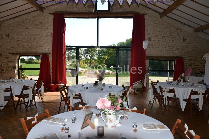Salle de réception lumineuse avec tables rondes décorées, grandes baies vitrées et vue sur un jardin verdoyant.