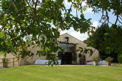 Vue depuis une porte vitrée sur un jardin avec des tables hautes et des chaises disposées près d'un bâtiment en pierre.