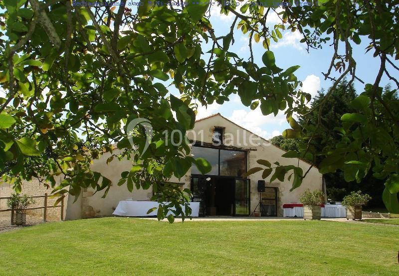 Vue d'une salle de réception en pierre avec une grande baie vitrée, entourée de verdure et d'arbres.