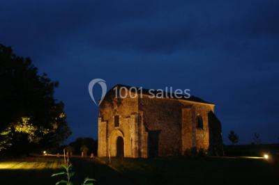 Vue depuis une porte vitrée sur un jardin avec des tables hautes et des chaises disposées près d'un bâtiment en pierre.
