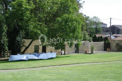 Vue depuis une porte vitrée sur un jardin avec des tables hautes et des chaises disposées près d'un bâtiment en pierre.