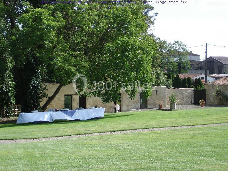 Pelouse verdoyante avec une longue table recouverte d'une nappe blanche, entourée d'arbres et de bâtiments en pierre.