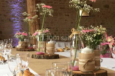 Vue depuis une porte vitrée sur un jardin avec des tables hautes et des chaises disposées près d'un bâtiment en pierre.