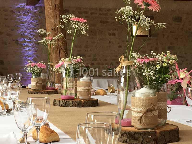 Décoration de table champêtre avec vases en verre, fleurs roses et blanches, nappes en toile de jute et rondins de bois.