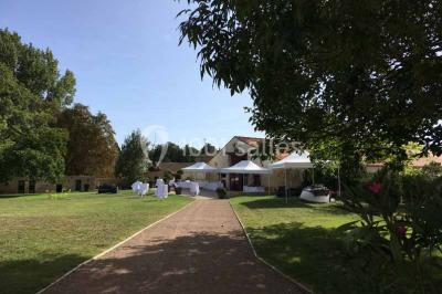 Vue depuis une porte vitrée sur un jardin avec des tables hautes et des chaises disposées près d'un bâtiment en pierre.