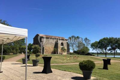 Vue depuis une porte vitrée sur un jardin avec des tables hautes et des chaises disposées près d'un bâtiment en pierre.