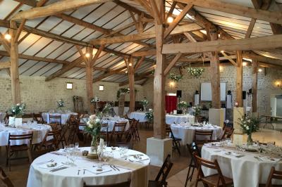 Vue depuis une porte vitrée sur un jardin avec des tables hautes et des chaises disposées près d'un bâtiment en pierre.