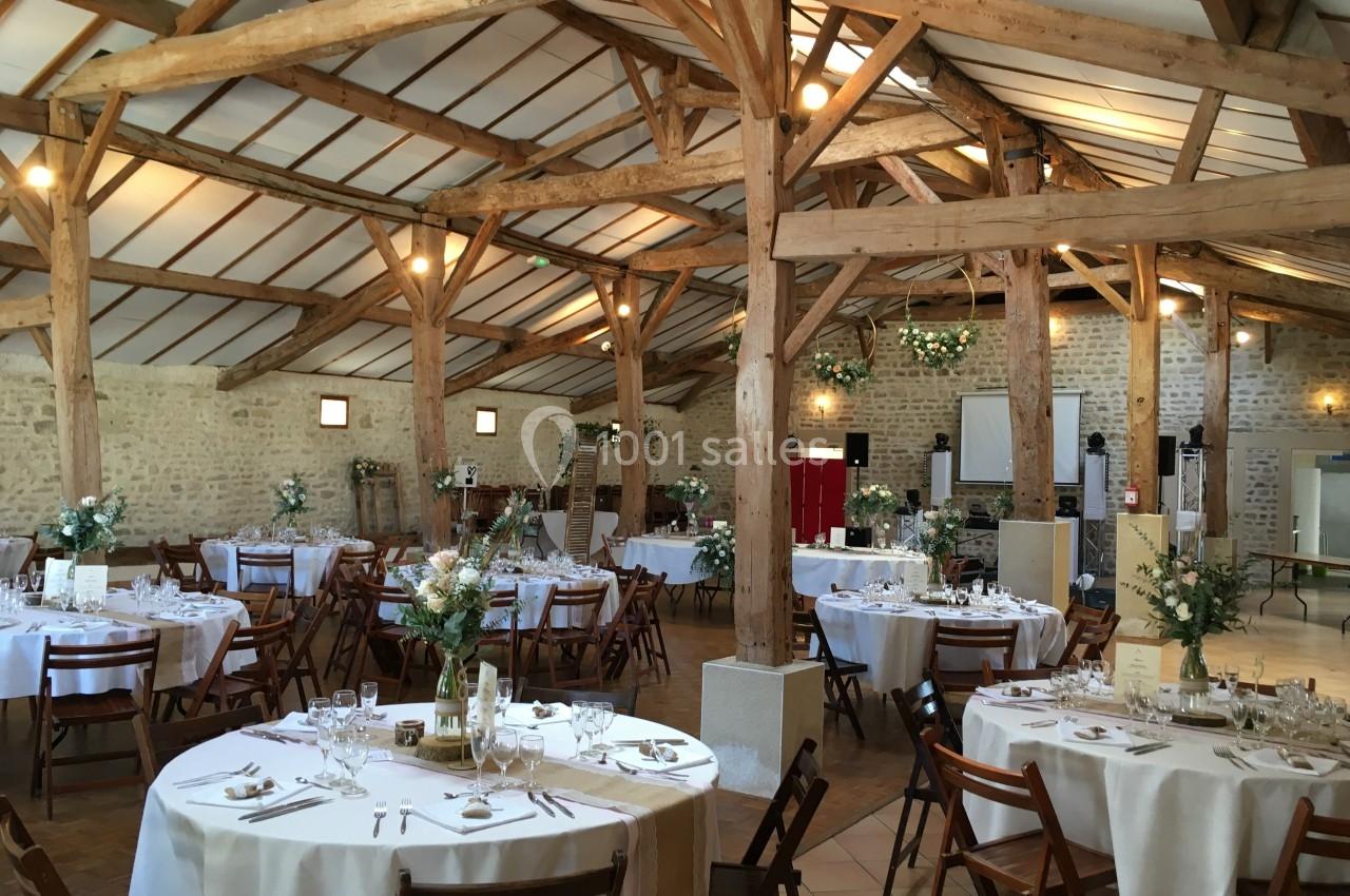 Salle de réception en pierre et bois avec tables rondes décorées pour un événement festif.