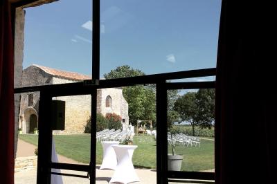 Vue depuis une porte vitrée sur un jardin avec des tables hautes et des chaises disposées près d'un bâtiment en pierre.
