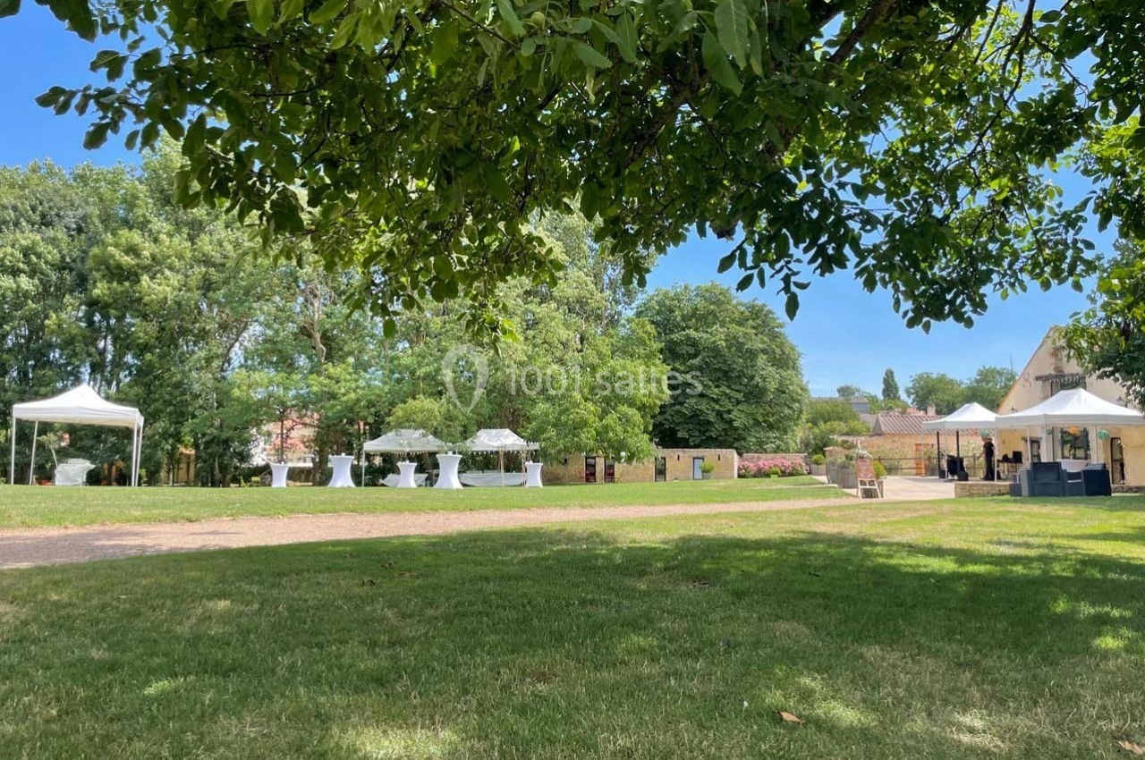 Pelouse verdoyante avec tentes blanches installées pour un événement en plein air, entourée d'arbres et de bâtiments.
