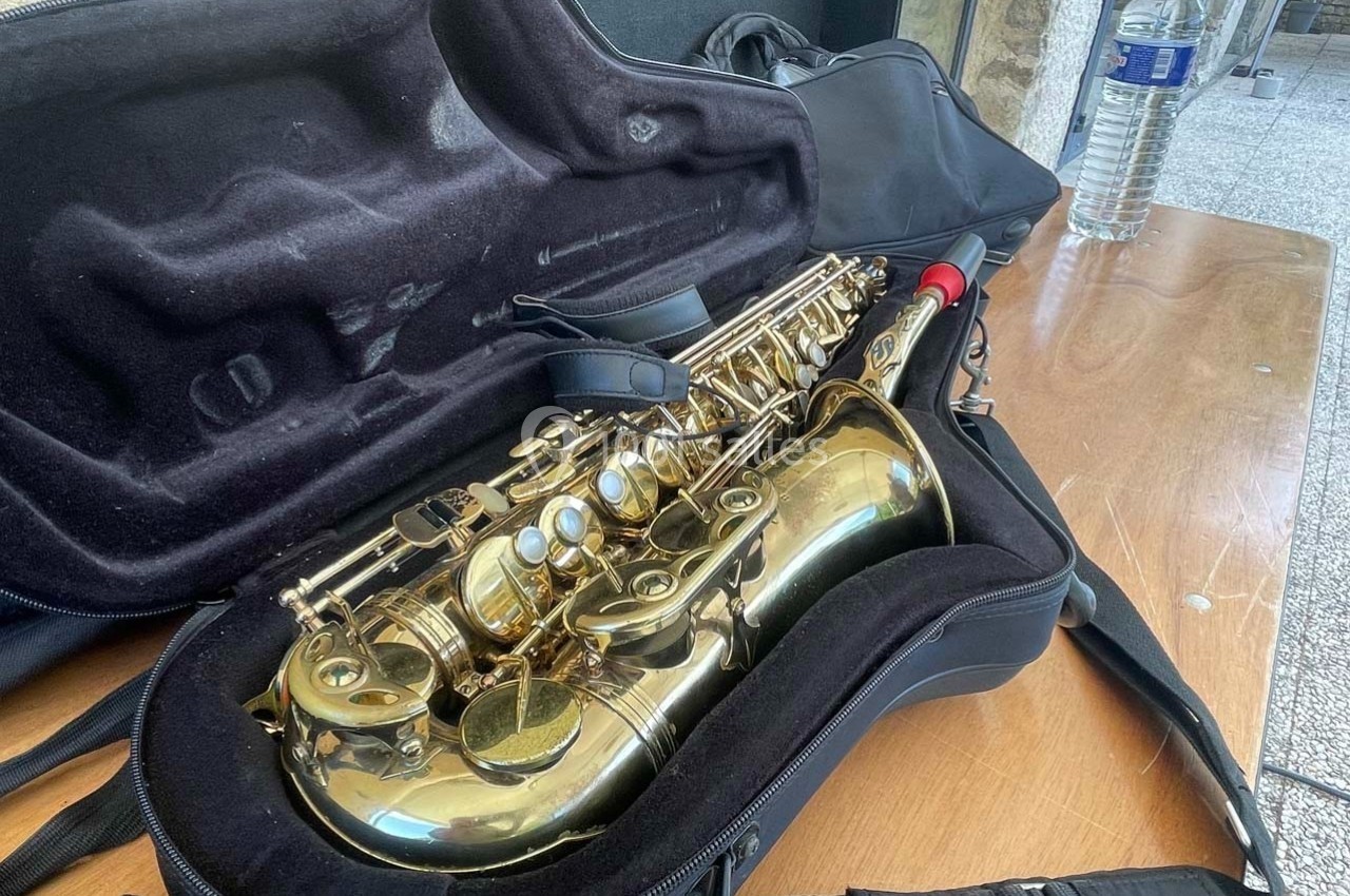 Saxophone doré rangé dans un étui ouvert, posé sur une table en bois à côté d'une bouteille d'eau.
