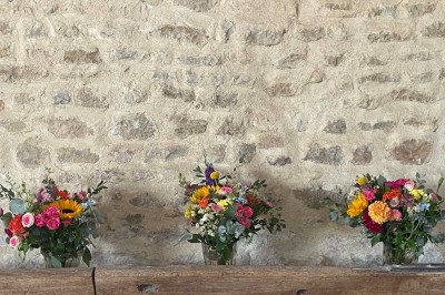 Miniature Location salle Le Bernard (Vendée) - La Grange du Prieuré #12 Centre de table avec des fleurs roses et blanches dans un vase doré, entouré de bougies et de verres sur une nappe blanche.