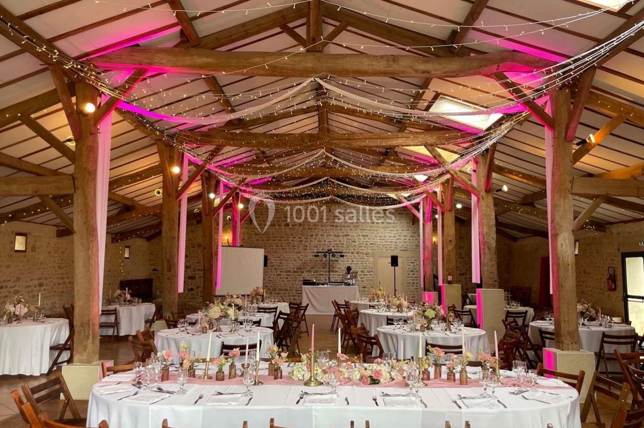 Salle de réception en pierre avec tables décorées, éclairage rose et guirlandes lumineuses suspendues.