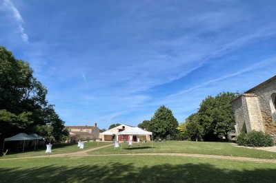 Miniature Location salle Le Bernard (Vendée) - La Grange du Prieuré #23 Centre de table avec des fleurs roses et blanches dans un vase doré, entouré de bougies et de verres sur une nappe blanche.