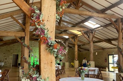 Miniature Location salle Le Bernard (Vendée) - La Grange du Prieuré #11 Centre de table avec des fleurs roses et blanches dans un vase doré, entouré de bougies et de verres sur une nappe blanche.
