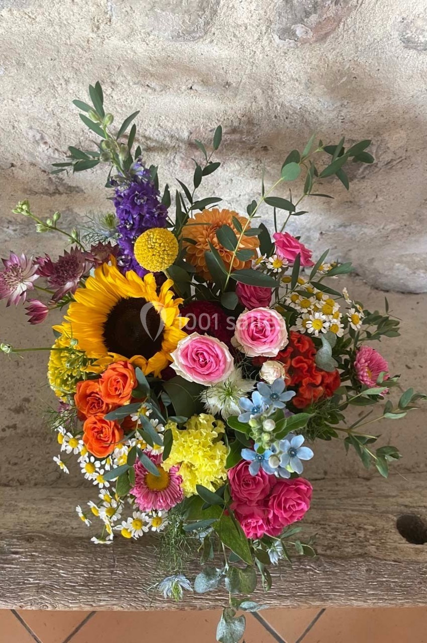 Bouquet coloré de fleurs variées, comprenant tournesol, roses, marguerites et feuillage, posé sur un banc en bois.