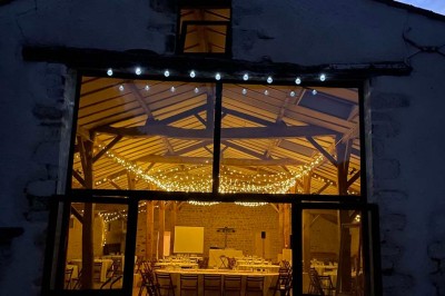 Miniature Location salle Le Bernard (Vendée) - La Grange du Prieuré #15 Centre de table avec des fleurs roses et blanches dans un vase doré, entouré de bougies et de verres sur une nappe blanche.