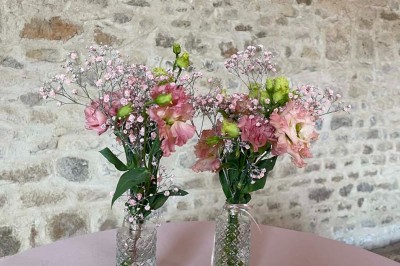 Miniature Location salle Le Bernard (Vendée) - La Grange du Prieuré #26 Centre de table avec des fleurs roses et blanches dans un vase doré, entouré de bougies et de verres sur une nappe blanche.