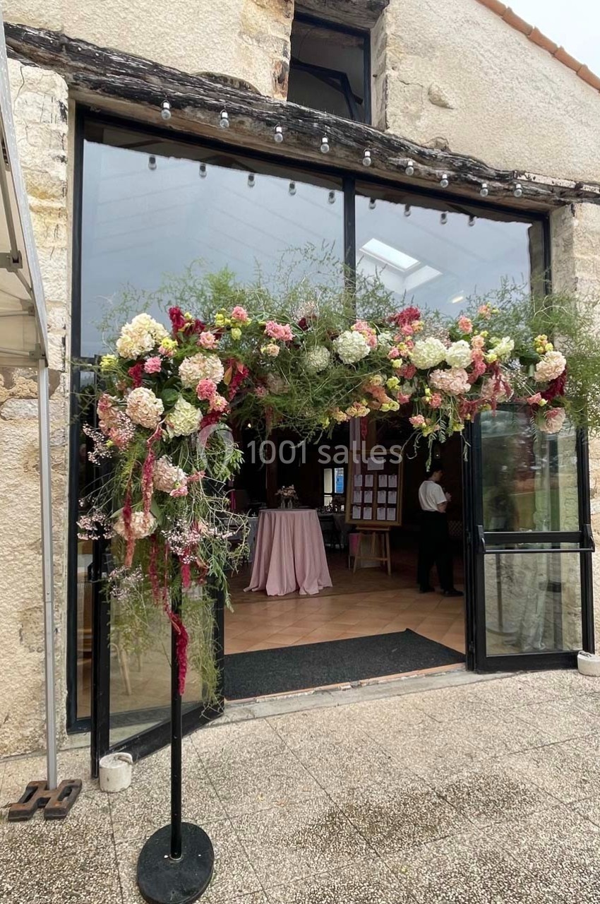 Entrée d'un bâtiment en pierre décorée d'une arche florale avec des fleurs colorées et feuillages.