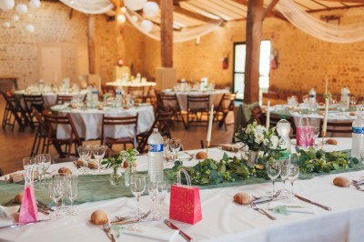 Miniature Location salle Le Bernard (Vendée) - La Grange du Prieuré #10 Centre de table avec des fleurs roses et blanches dans un vase doré, entouré de bougies et de verres sur une nappe blanche.