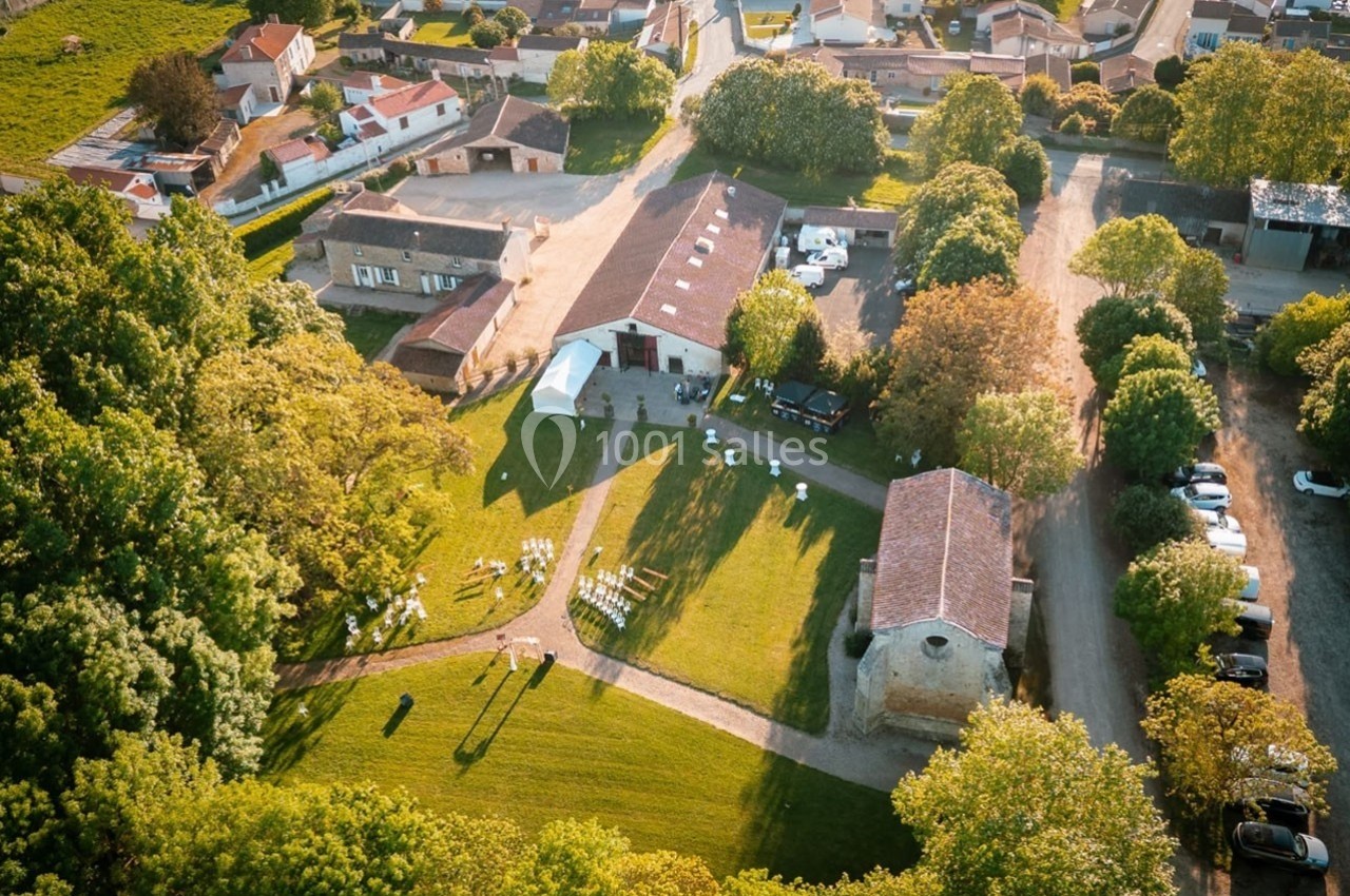 Vue aérienne d'un domaine rural avec bâtiments, espaces verts et installation de chaises en extérieur.