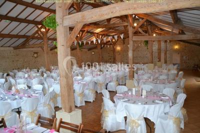 Vue depuis une porte vitrée sur un jardin avec des tables hautes et des chaises disposées près d'un bâtiment en pierre.