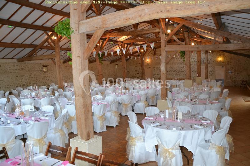 Salle de réception décorée avec des tables rondes, nappes blanches et chaises ornées de nœuds beige.