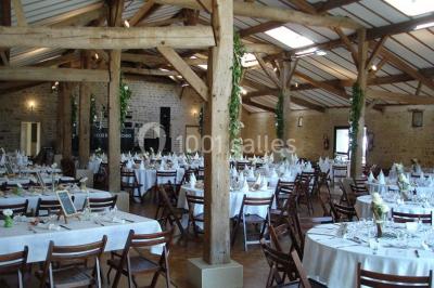 Vue depuis une porte vitrée sur un jardin avec des tables hautes et des chaises disposées près d'un bâtiment en pierre.