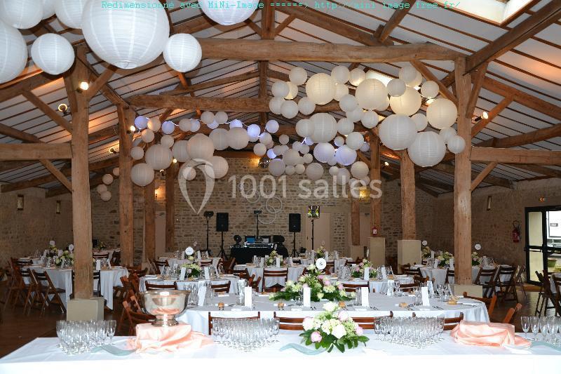 Salle de réception décorée avec des lanternes blanches suspendues, tables dressées et arrangements floraux.