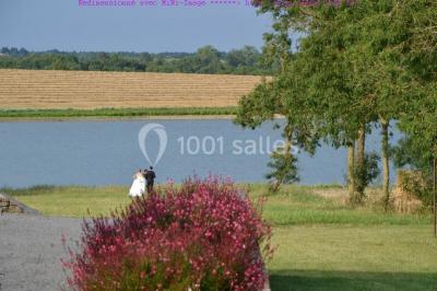 Vue depuis une porte vitrée sur un jardin avec des tables hautes et des chaises disposées près d'un bâtiment en pierre.