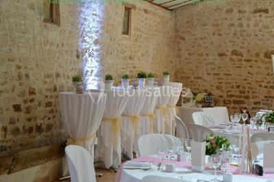 Vue depuis une porte vitrée sur un jardin avec des tables hautes et des chaises disposées près d'un bâtiment en pierre.