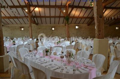 Vue depuis une porte vitrée sur un jardin avec des tables hautes et des chaises disposées près d'un bâtiment en pierre.